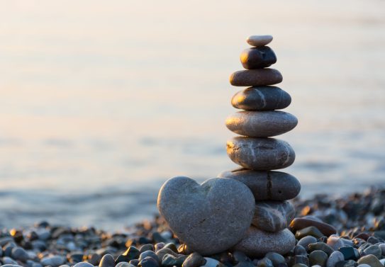Grey stone in shape of heart in front of balanced stones on still water background